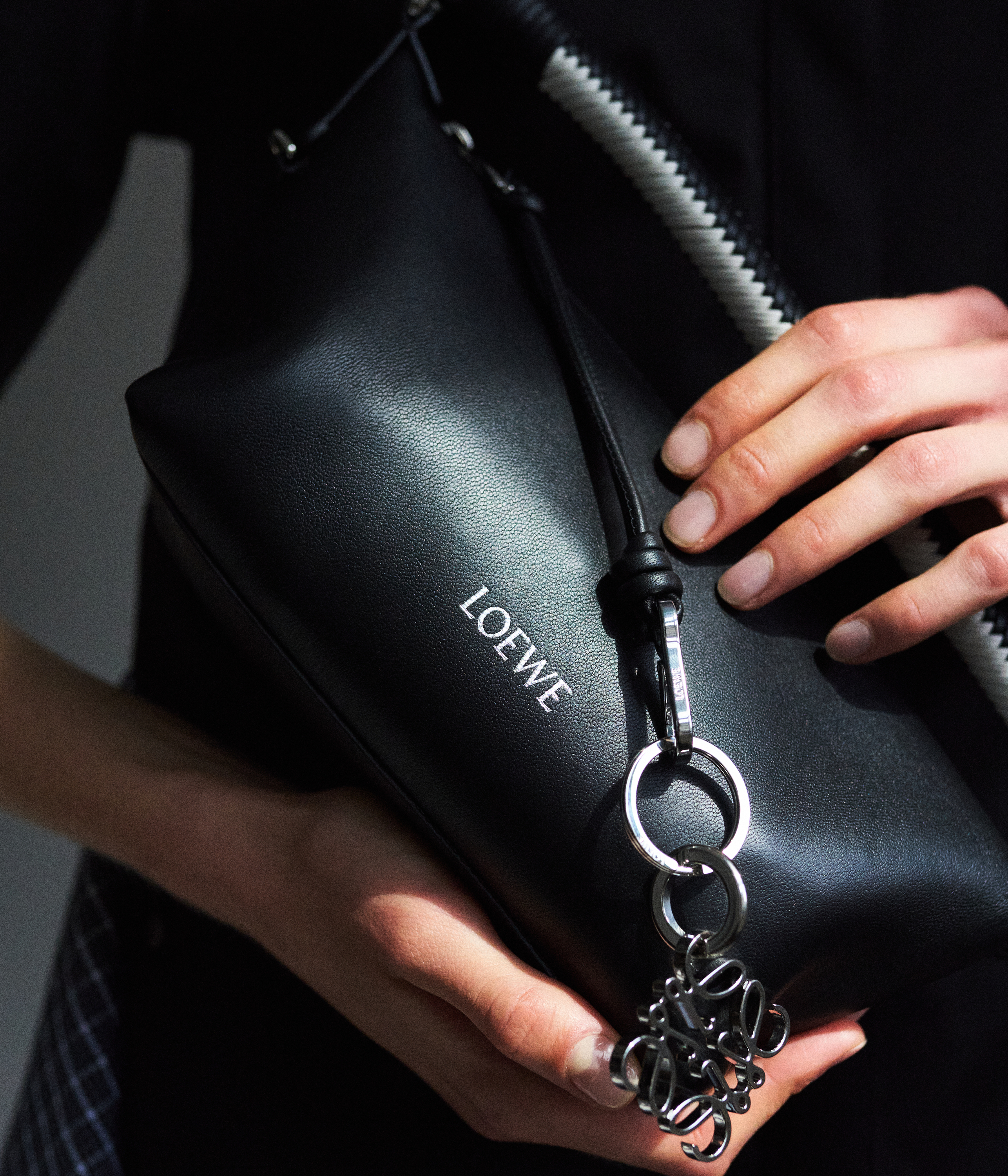 Schwarze Loewe-Umhängetasche aus Leder mit silbernen Ringen und geprägtem Logo in einer Hand.