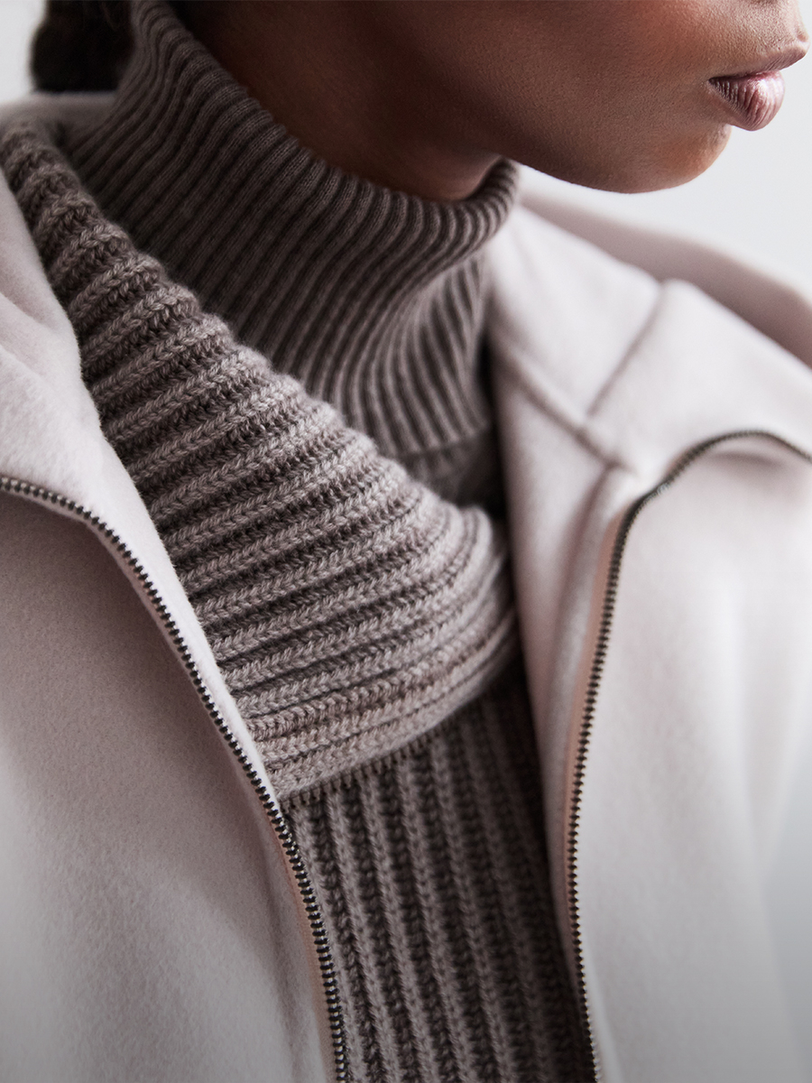 Detailaufnahme einer Person im grobgestrickten Turtleneck-Pullover und heller Jacke von Iris von Arnim.